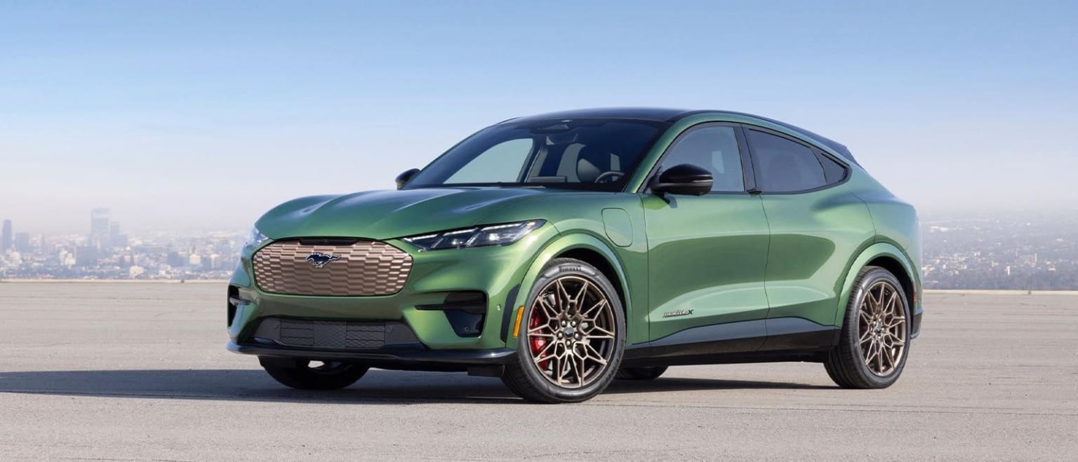 Green electric SUV on road with city skyline and blue sky in background.