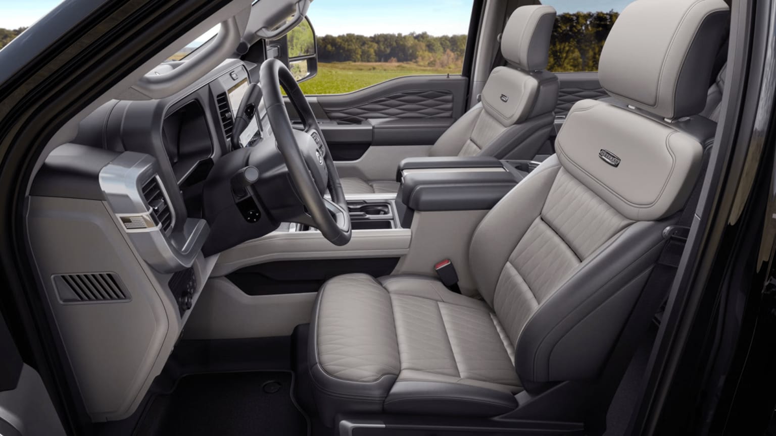 Interior of a modern truck with light gray leather seats and detailed dashboard, overlooking a grassy field and trees.