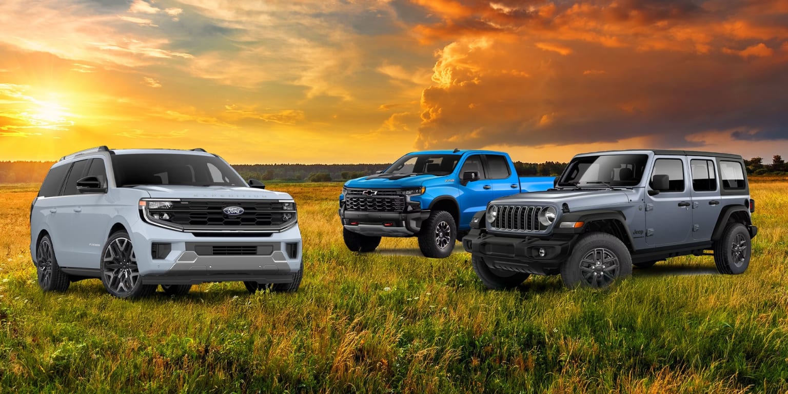 Three off-road vehicles in a grassy field under a dramatic sunset sky with billowing clouds.