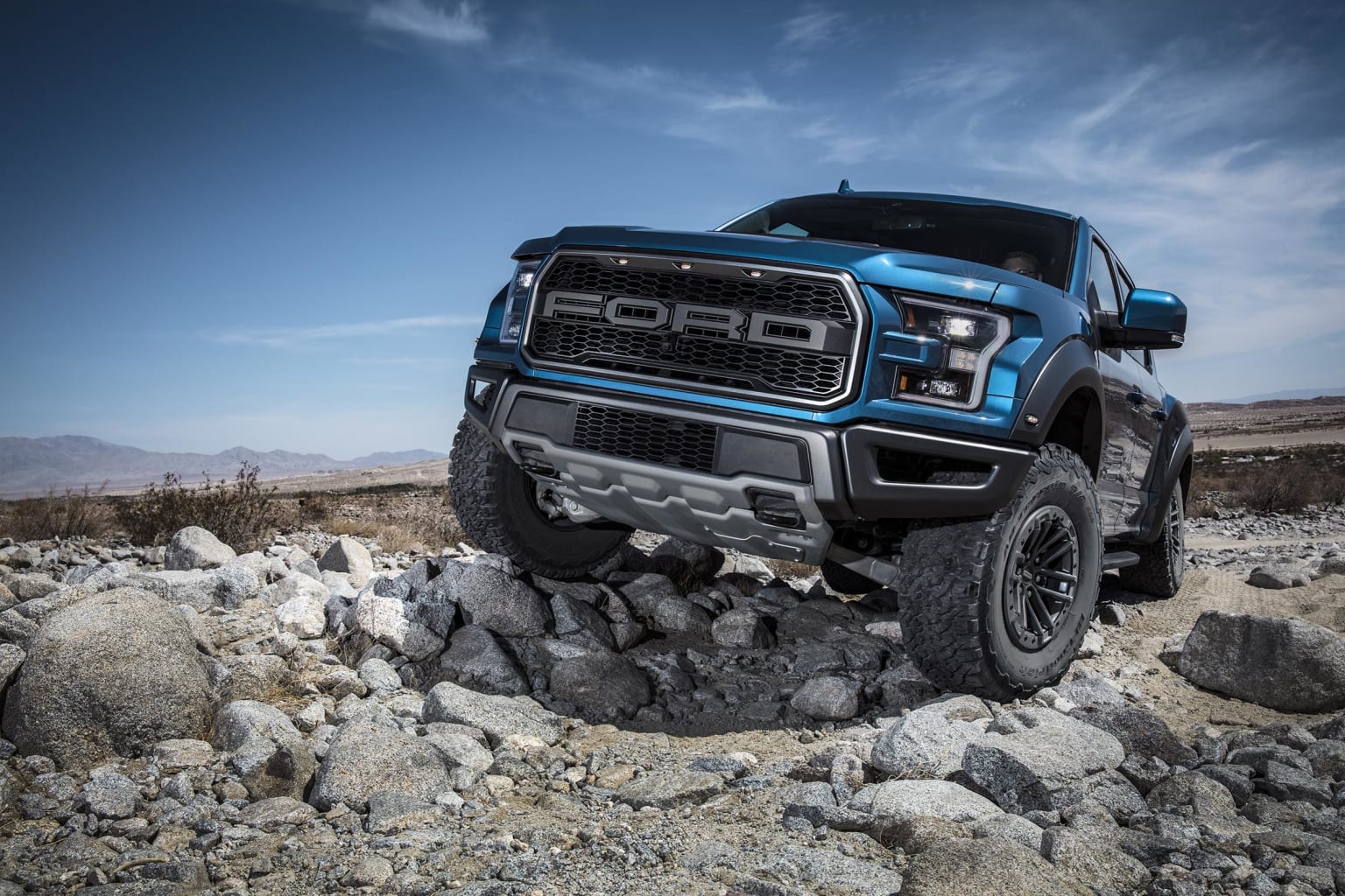 a blue truck parked on top of a pile of rocks in the middle of a desert area with a blue sky in the background