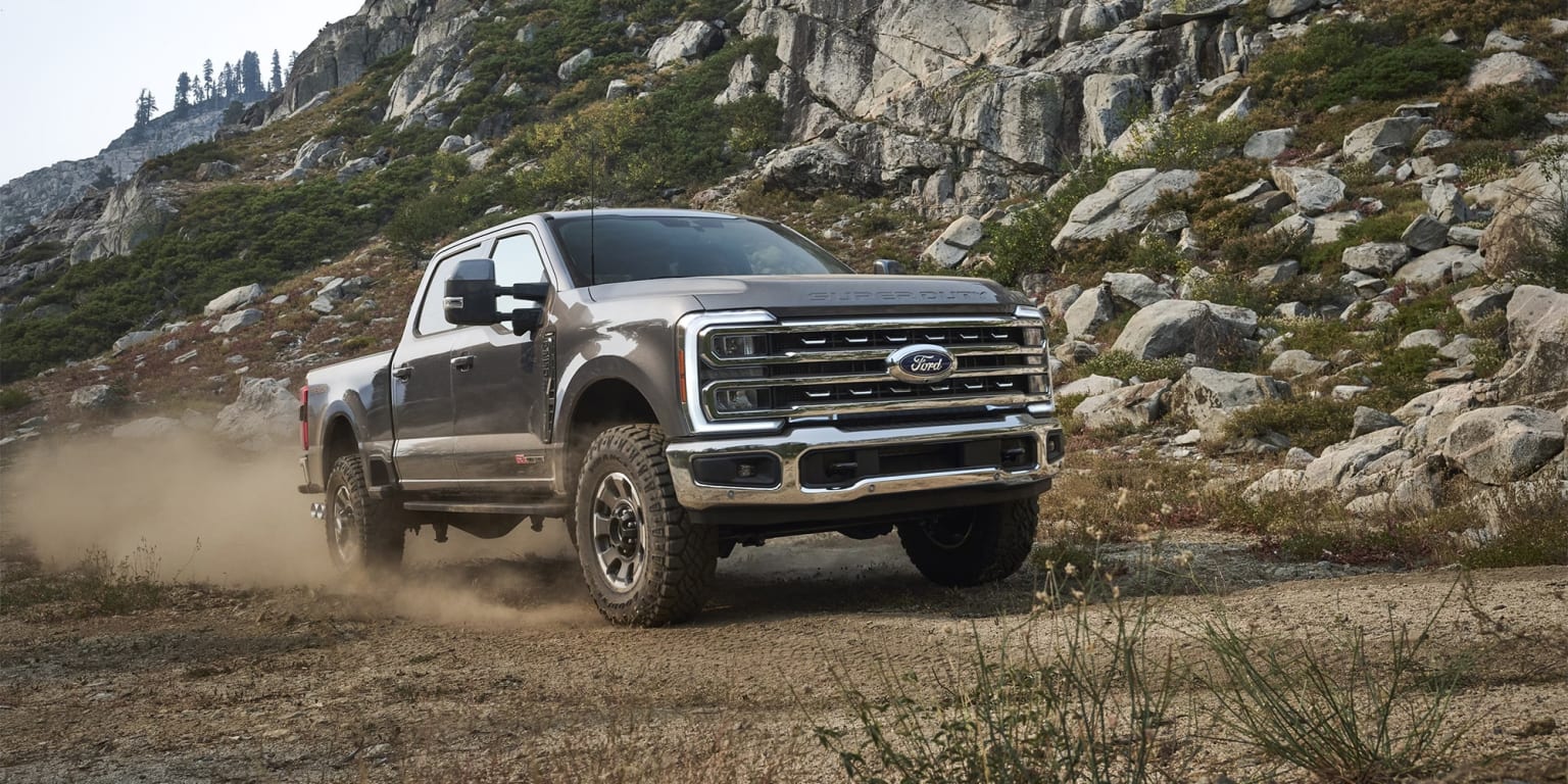 An off-road pickup truck navigating rocky terrain and kicking up dust.