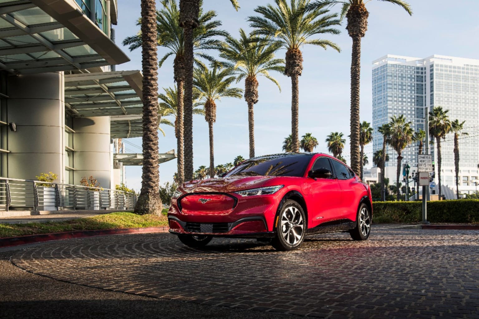 a red car parked in front of palm trees in front of a building with tall buildings in the background