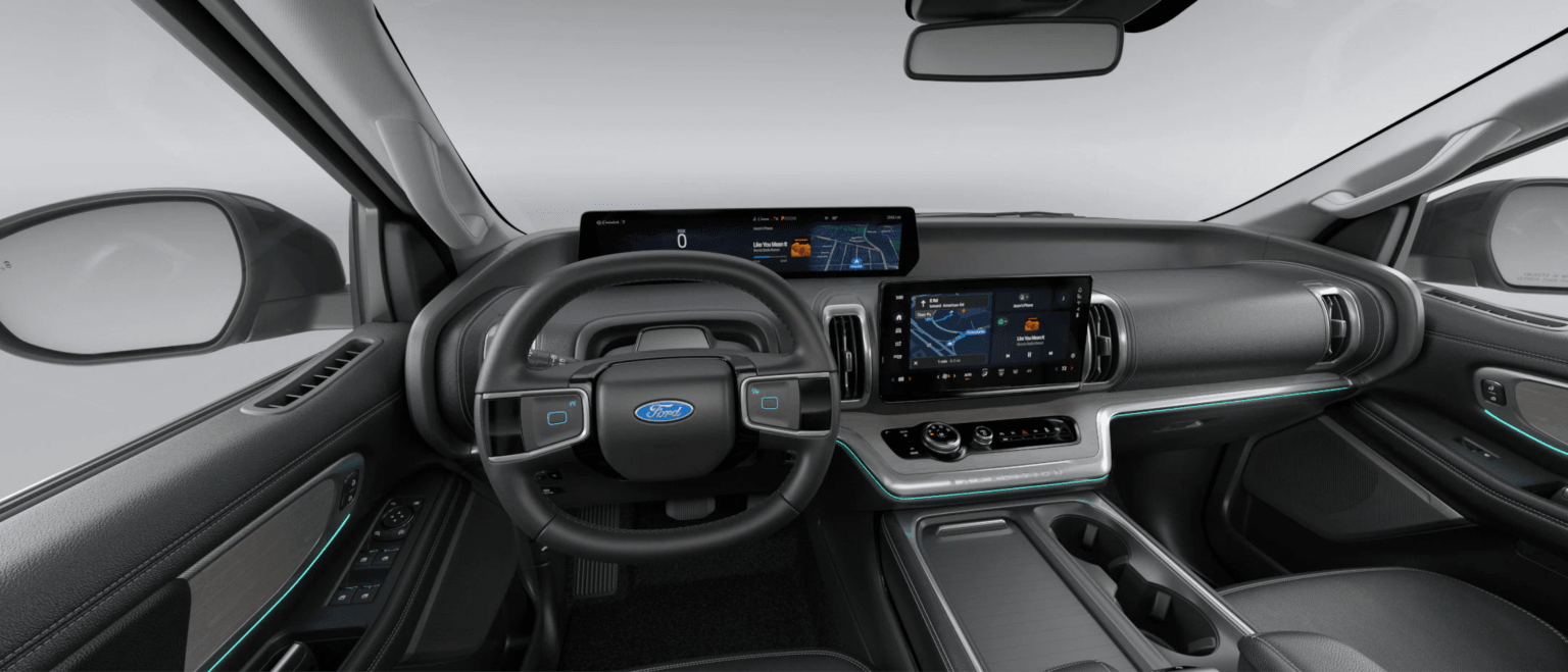 The image features a modern car's dashboard with a steering wheel and two large screens in the foreground, and the car's interior with a rearview mirror and side windows in the background.