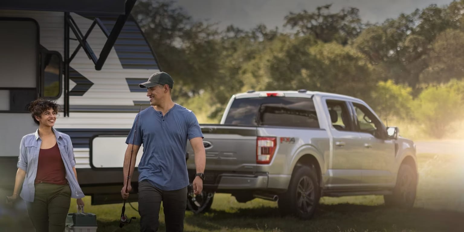 a man and a woman walking in front of a truck with a camper trailer in the back ground