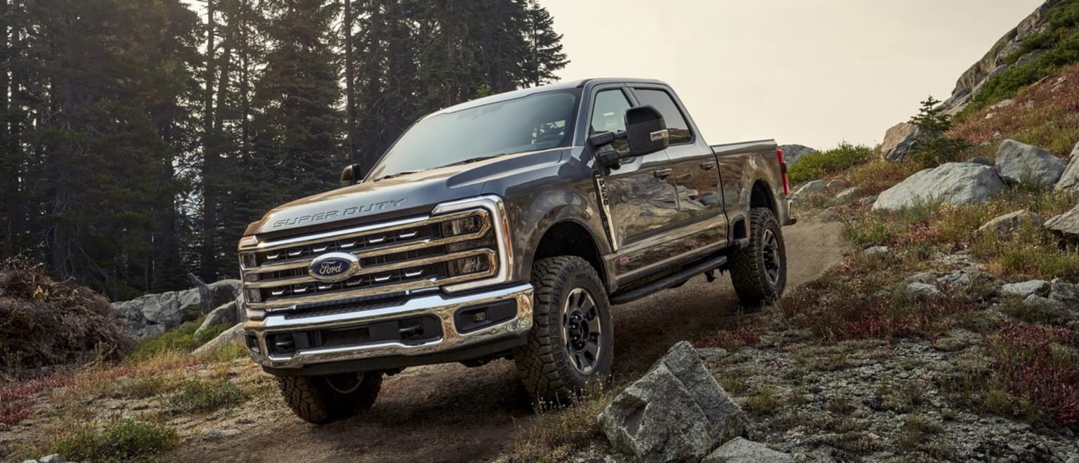 A rugged pickup truck navigates over rocky terrain, surrounded by a lush, forested landscape.