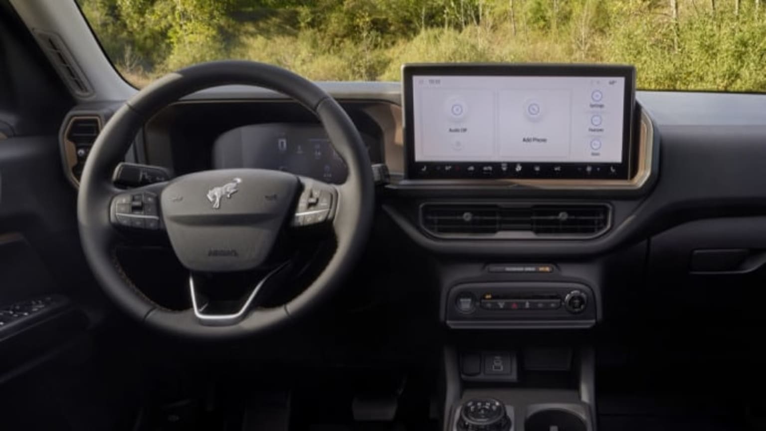 A modern car's dashboard with a large touchscreen display is visible in the foreground, while a blurred green landscape is seen through the windshield in the background.