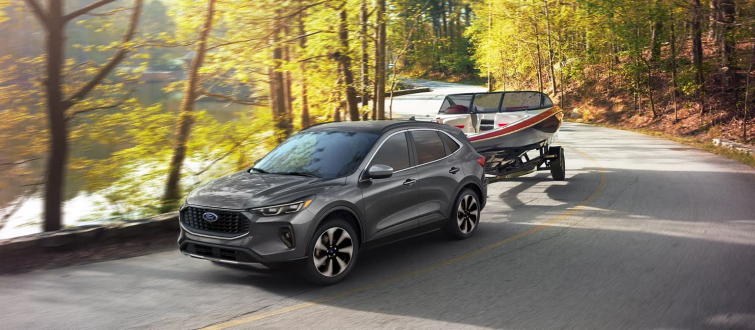 An SUV is driving down a winding road surrounded by a lush, autumnal forest with vibrant yellow and green foliage.