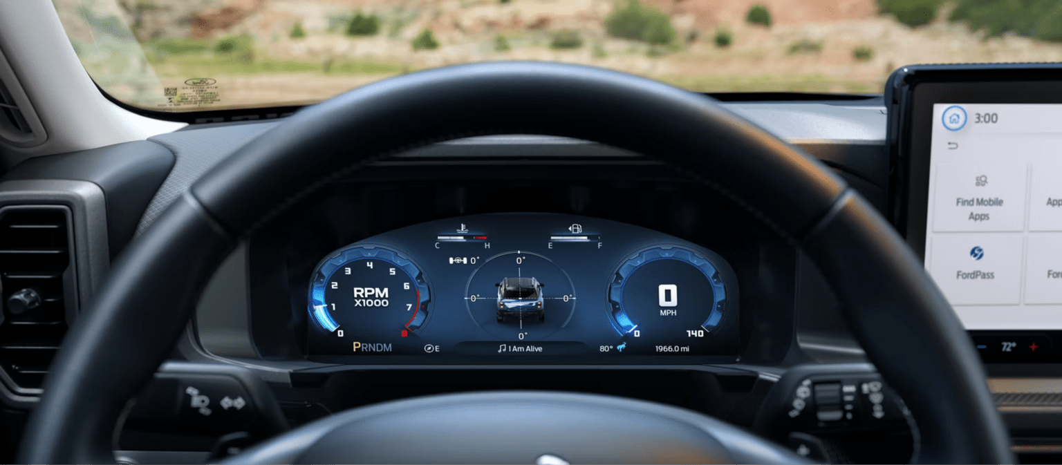 An image of a car's digital dashboard displaying driving information, with a blurred arid landscape visible through the windshield in the background.