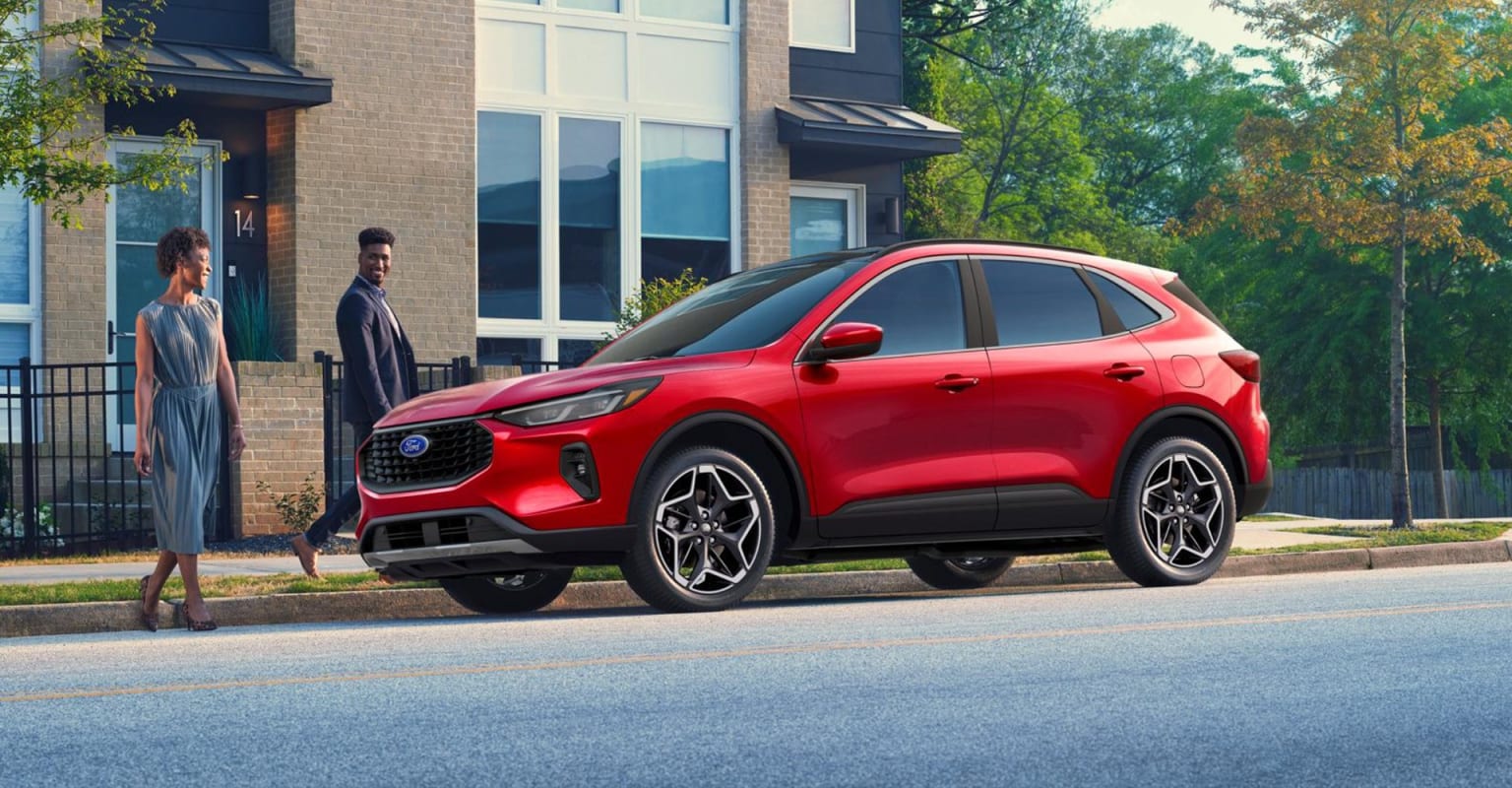 Red SUV parked in front of a modern brick building with two people nearby.