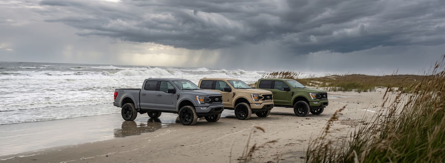 Three pickup trucks on a beach with stormy sky and crashing waves