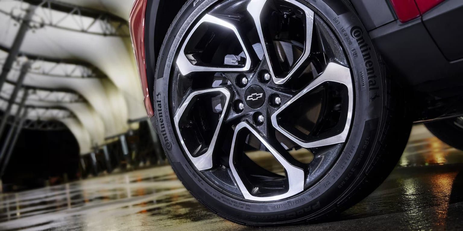 A black sedan parked in a garage with its wheel and tire visible, and the car is parked on a wet surface.