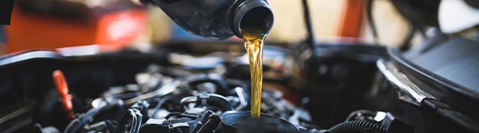 Close-up view of fresh engine oil being poured into a car's engine, with mechanical components in the background.