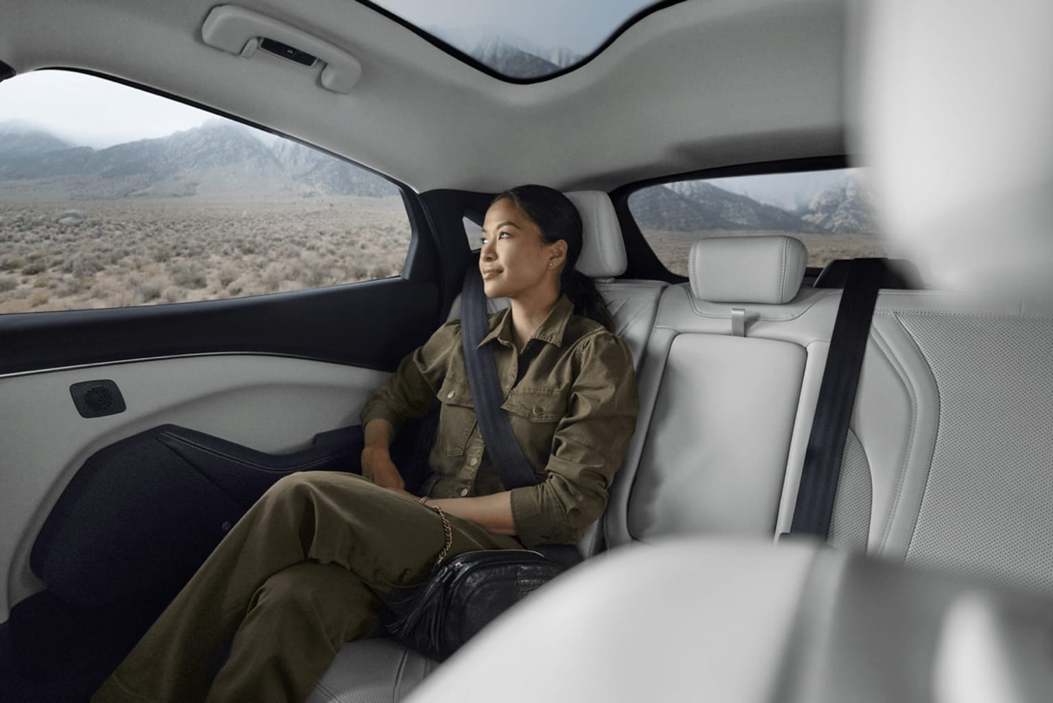 A person in military-style clothing sitting in the backseat of a vehicle with a desert landscape visible through the windows.