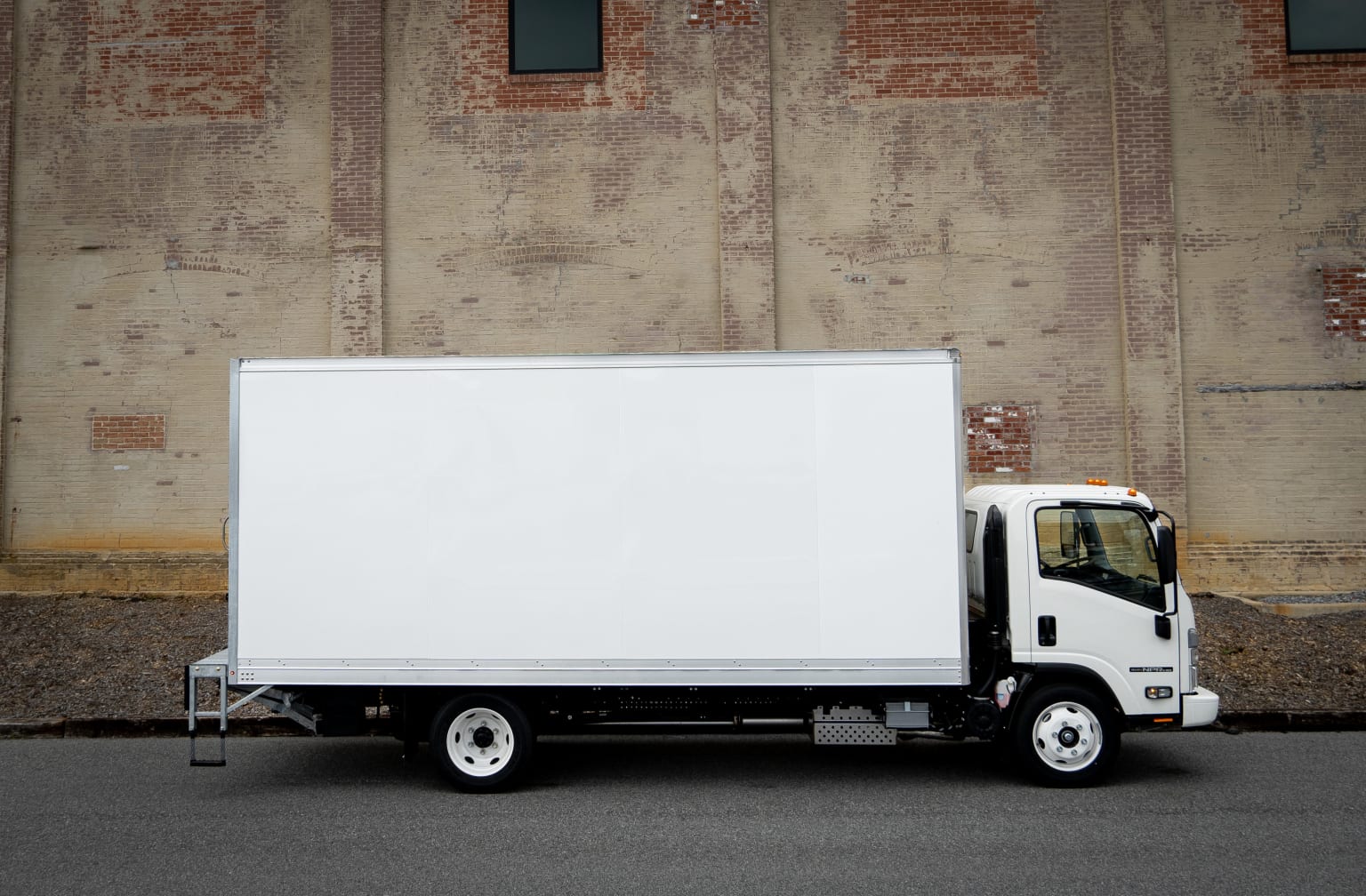 A white delivery truck parked in front of a brick wall, ready for advertising or branding.