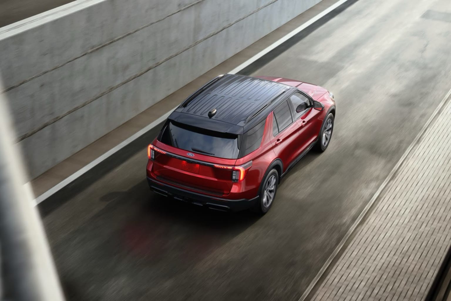 A red SUV driving down a concrete road with a gray concrete wall in the background.