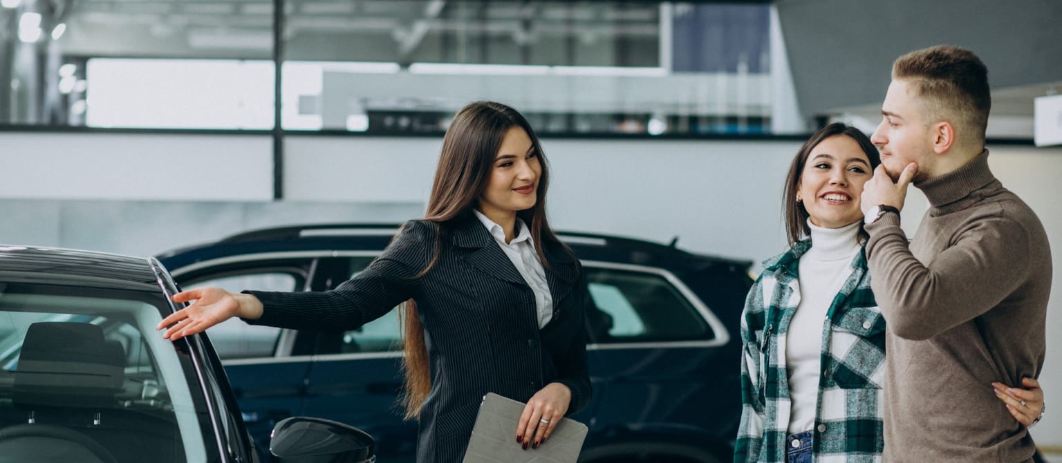 a man and a woman standing next to a car talking on a cell phone while another woman holds a folder in her hand