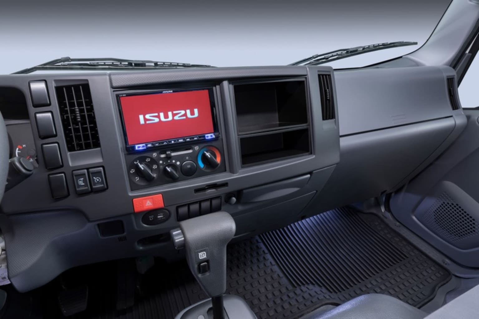 The image shows the interior of a truck, with a large display screen prominently featuring a logo in the center of the dashboard.