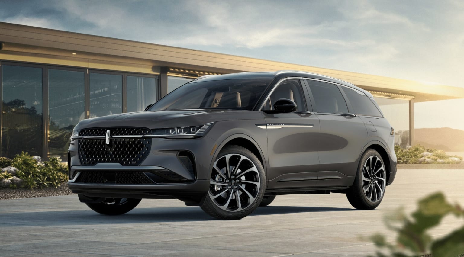 A sleek and modern-looking SUV with a bold grille and distinctive design elements parked in front of a building with large glass windows, set against a cloudy sky.