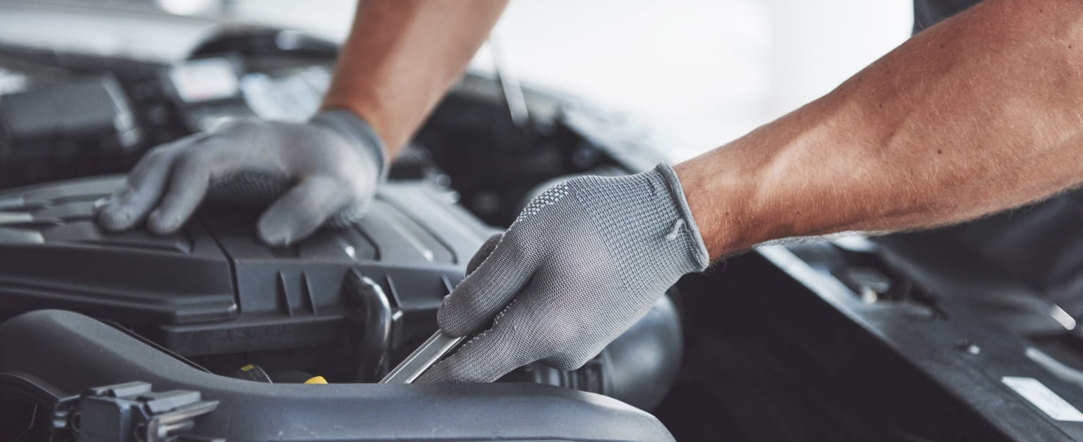 a man working on a car engine with a glove on his hand and a wrench in his other hand