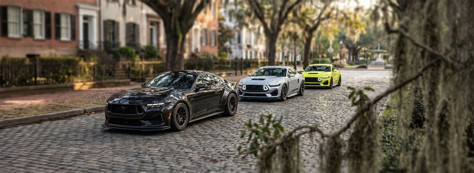 High-performance SUVs parked on a cobblestone street lined with trees and historic buildings.
