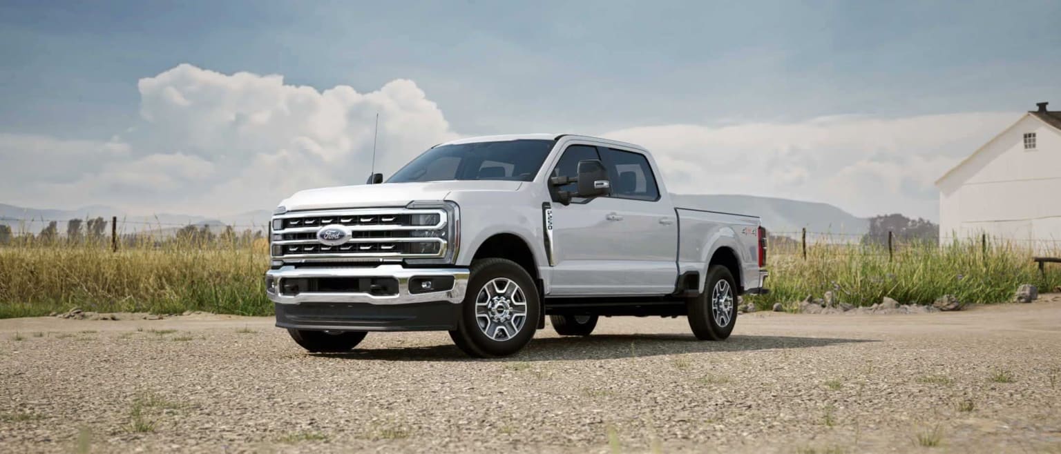 A white pickup truck in a grassy field with a cloudy sky in the background.