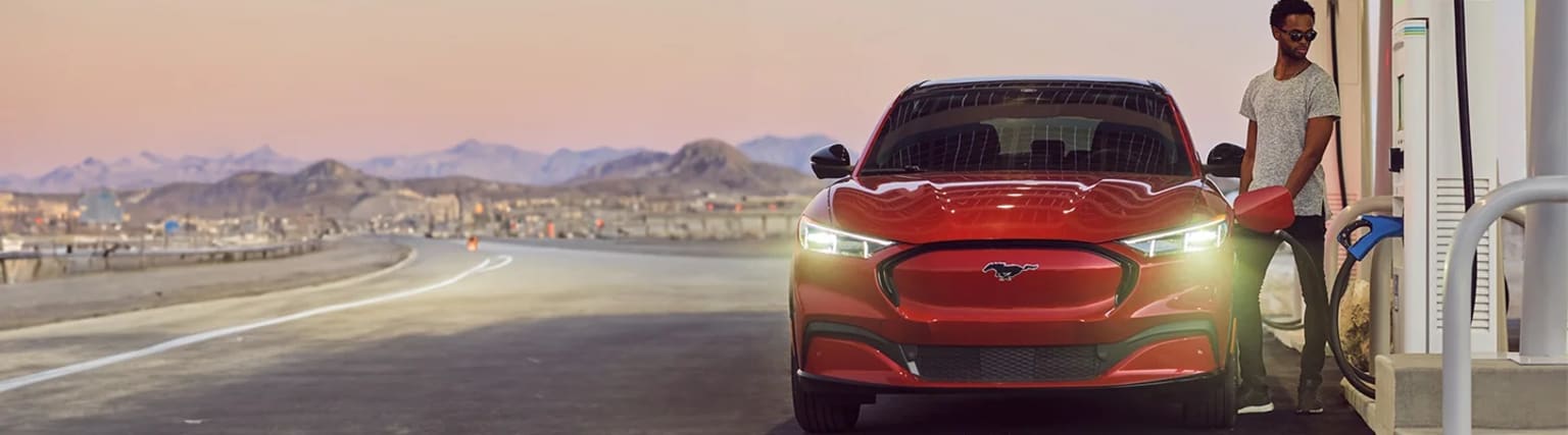 A red sports car with a distinctive grille design parked on a winding road, with a mountainous landscape visible in the background.