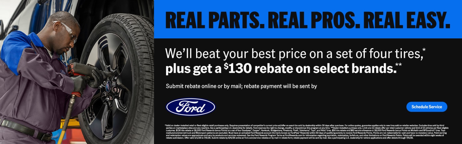 A mechanic working on a tire in the foreground with a tire rebate advertisement in the background.