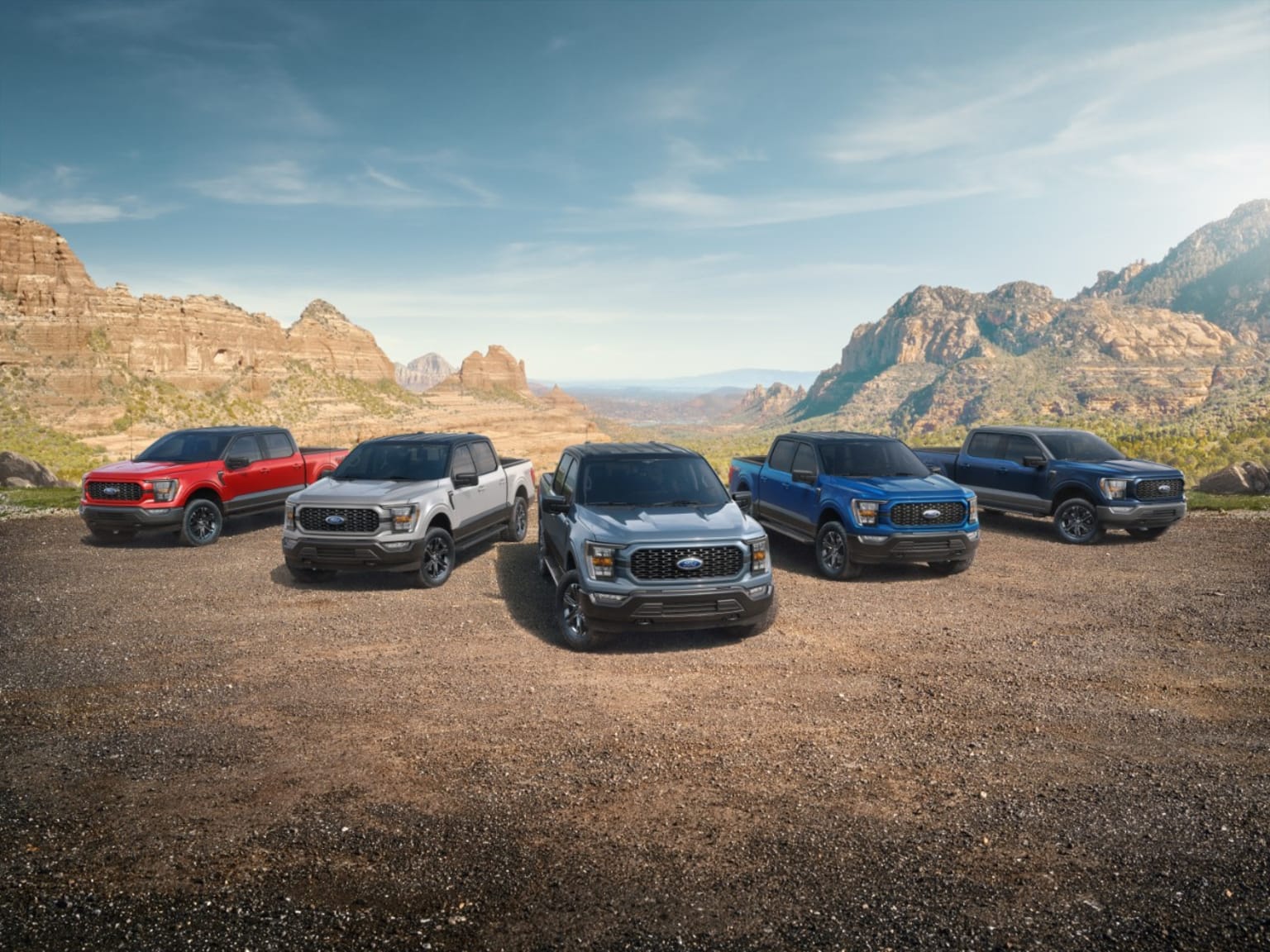 a group of four pickup trucks parked on a dirt road in front of a mountain range with mountains in the background