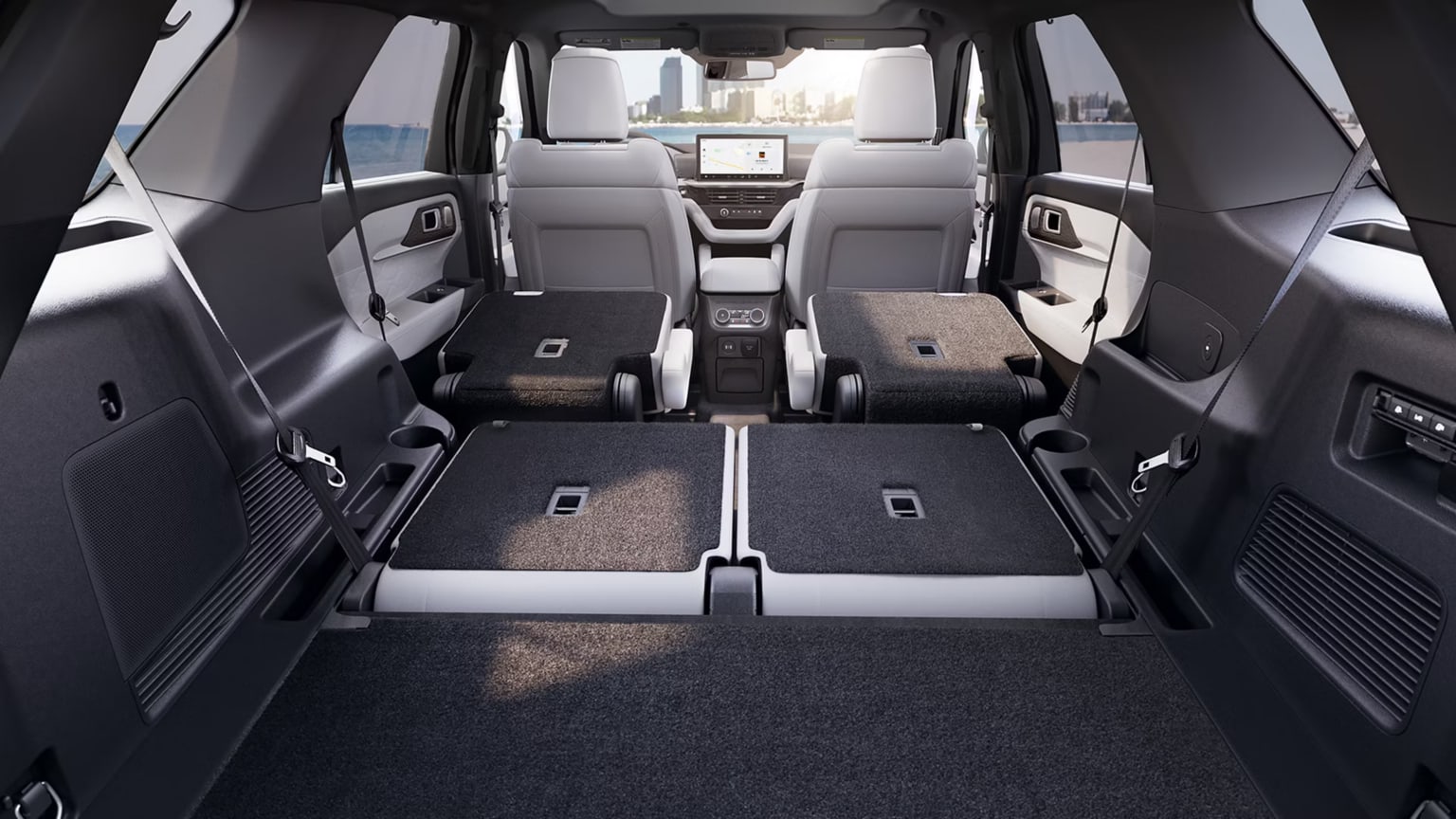 Spacious cargo area of a modern vehicle with folded rear seats, leading toward the front seats and city skyline visible through the windshield.