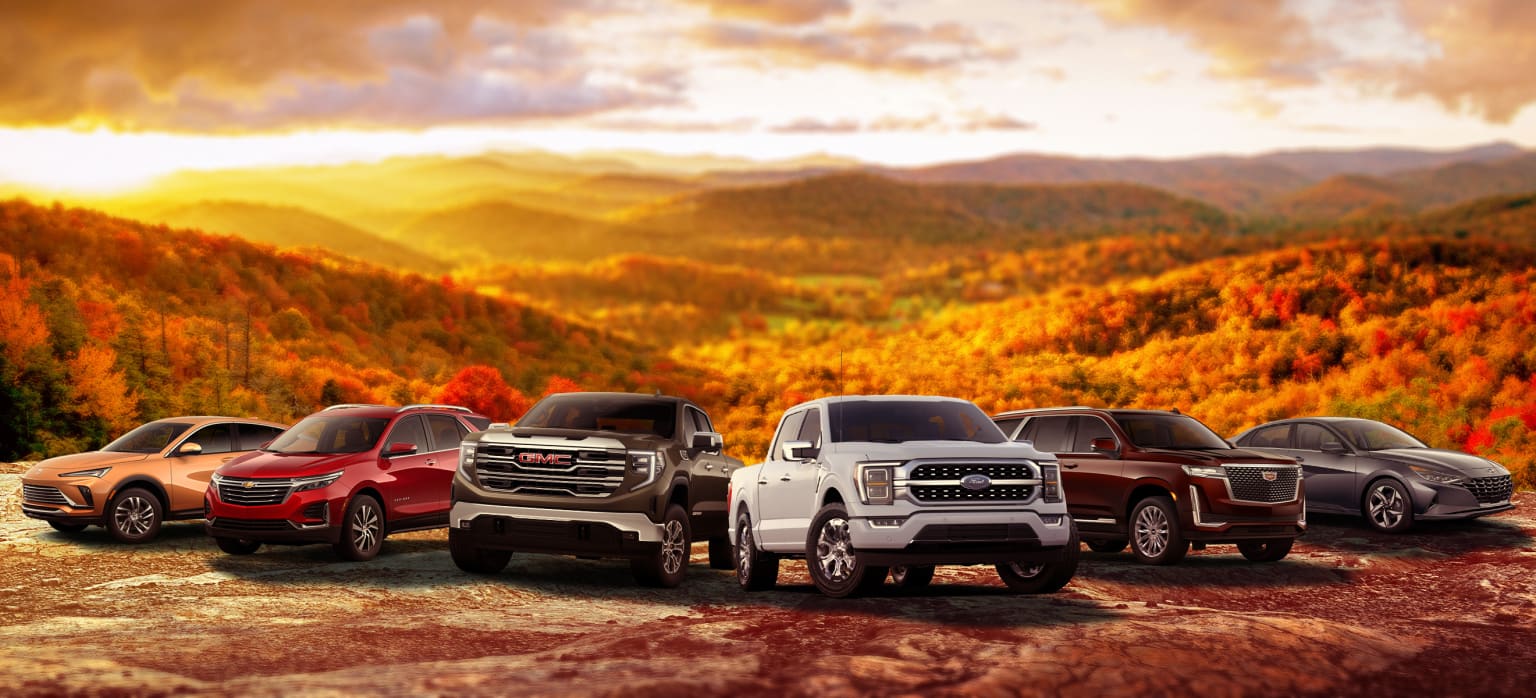 Rugged pickup trucks parked on a rocky outcrop in a picturesque autumn landscape with mountains and forests in the background, illuminated by the setting sun.