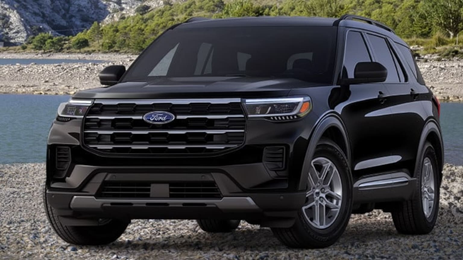 A black SUV is parked on a rocky shore with a body of water and hills in the background.