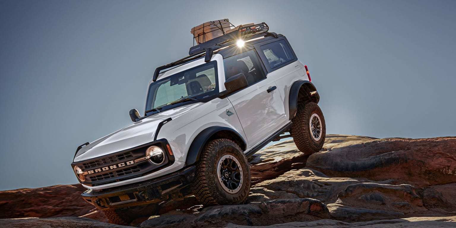 a white four - door suv with a roof rack is on a rocky surface with the sun shining on the rocks