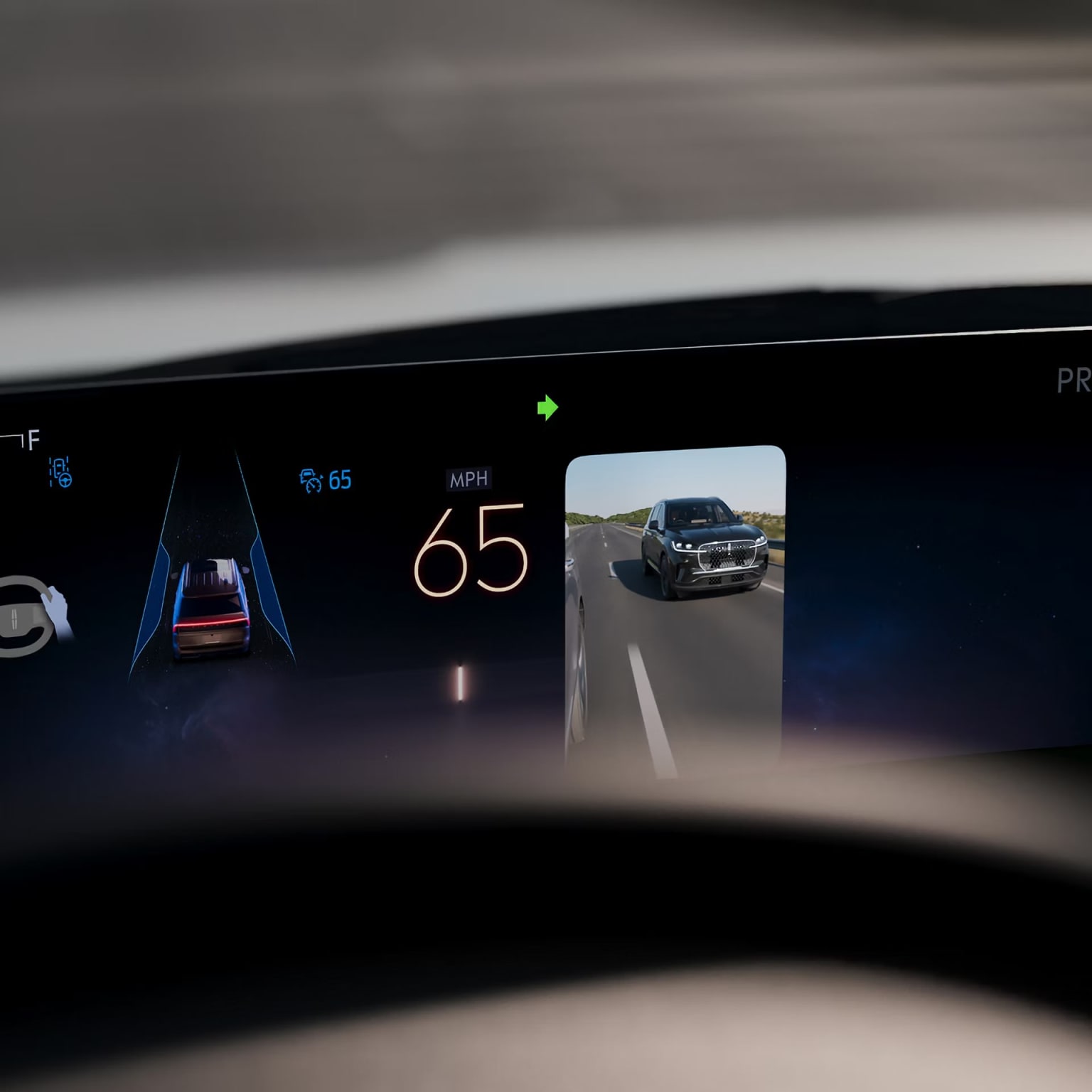 Image of a vehicle dashboard displaying a speedometer showing a speed of 65 mph and a camera feed in the center showing a truck on the road.