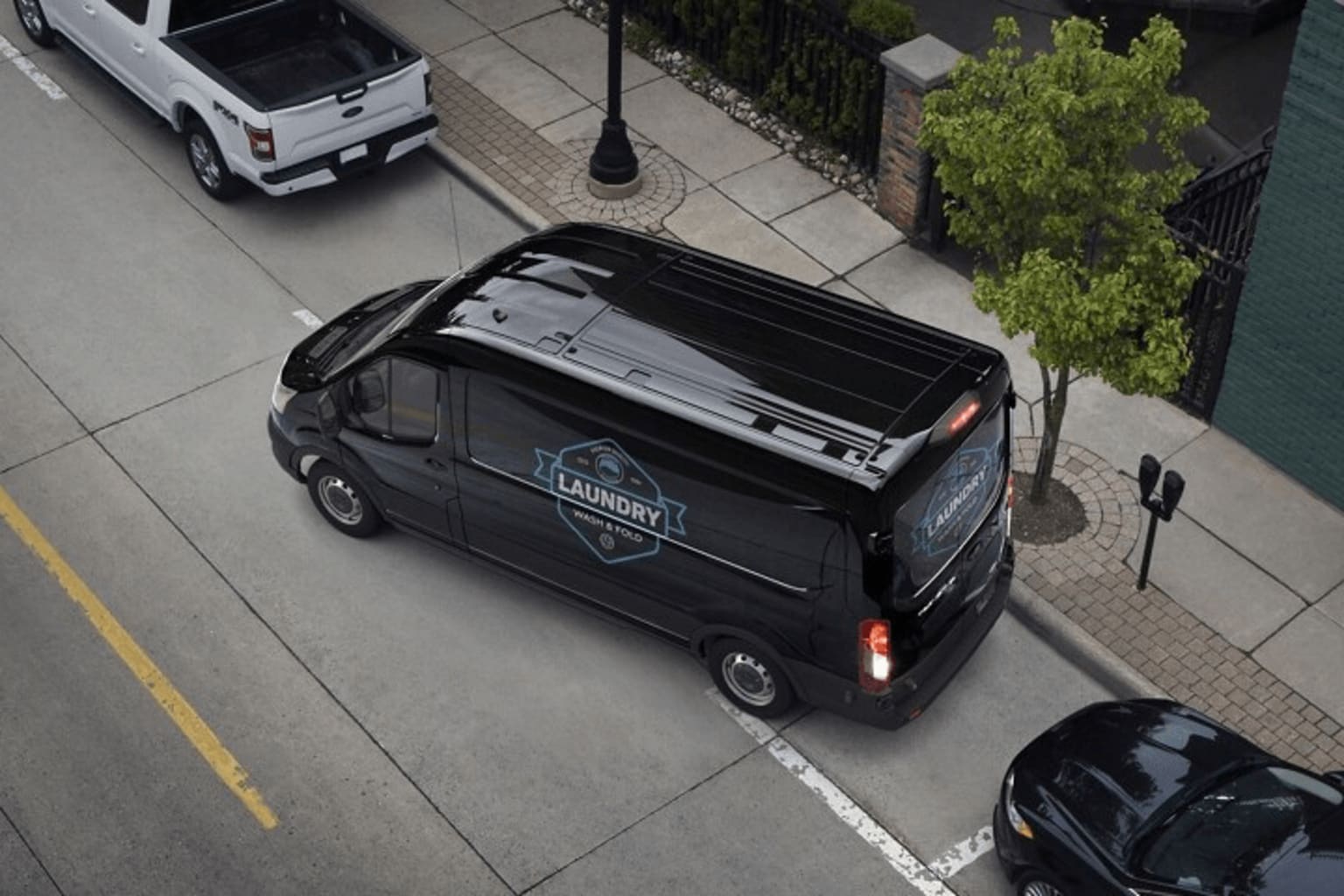 A black van with a Laundry logo parked on a sidewalk, surrounded by trees and other vehicles in the background.