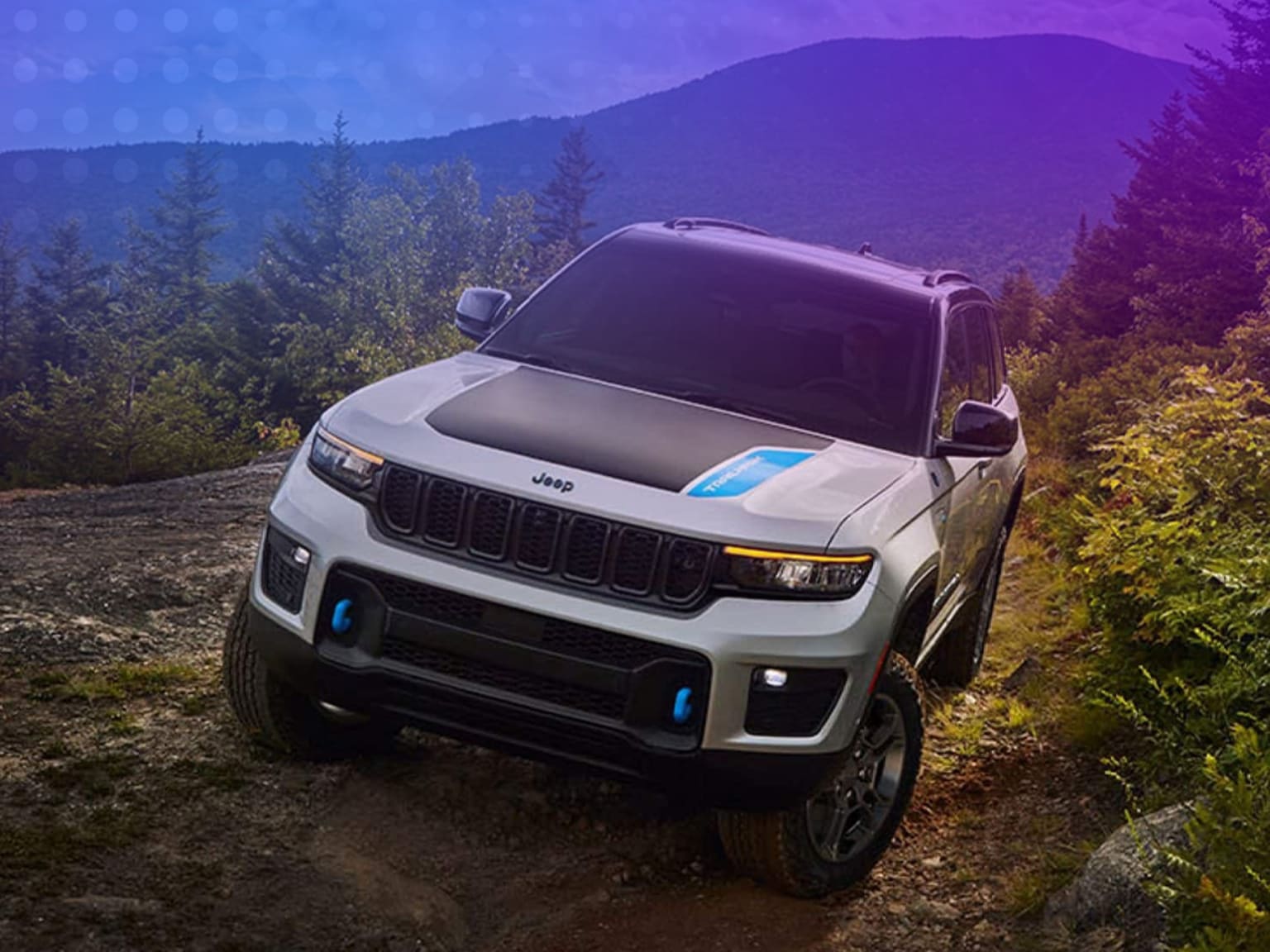 Off-road vehicle on a dirt path surrounded by lush forests and mountains in the distance.