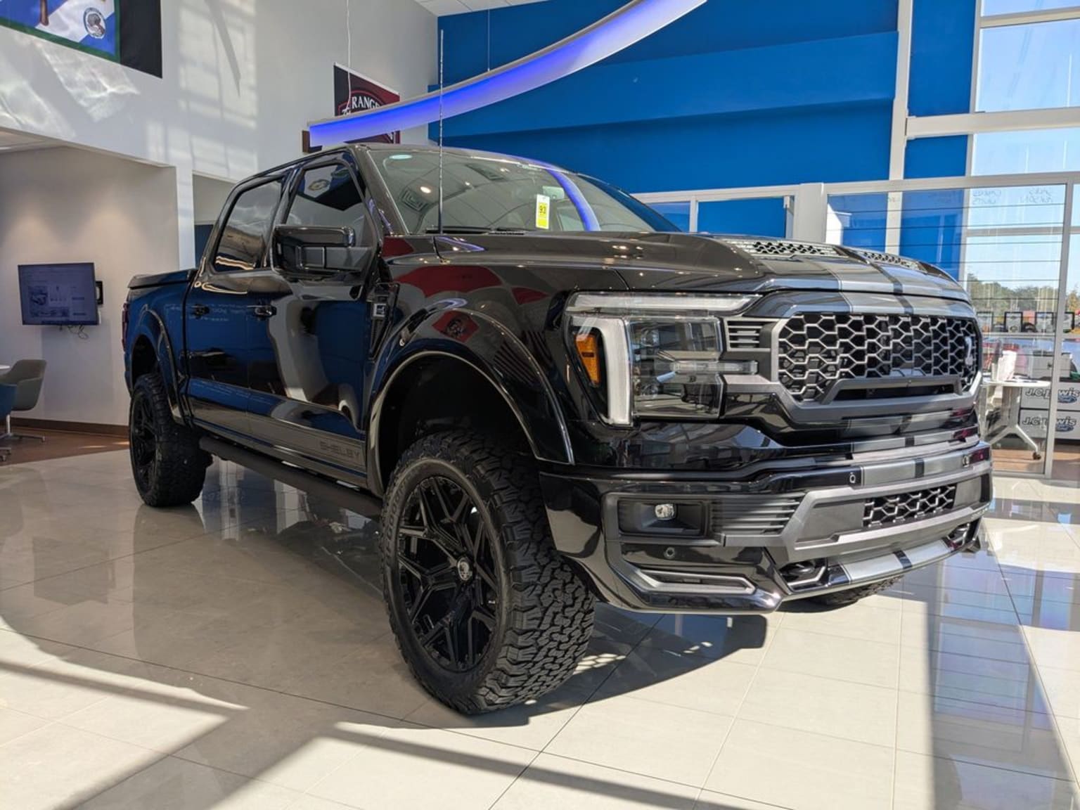 A large, black, heavily modified pickup truck displayed in a modern, brightly lit showroom with a blue and white background.