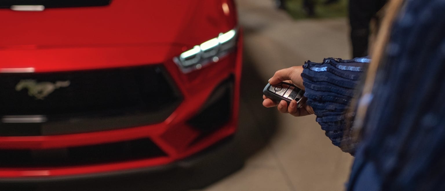 A hand holding a remote control in front of a red vehicle.