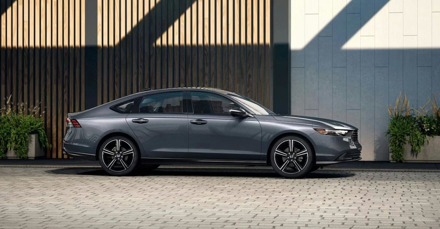 A gray sedan parked on a textured gray pavement in front of a modern building with vertical wooden slats and a concrete wall.