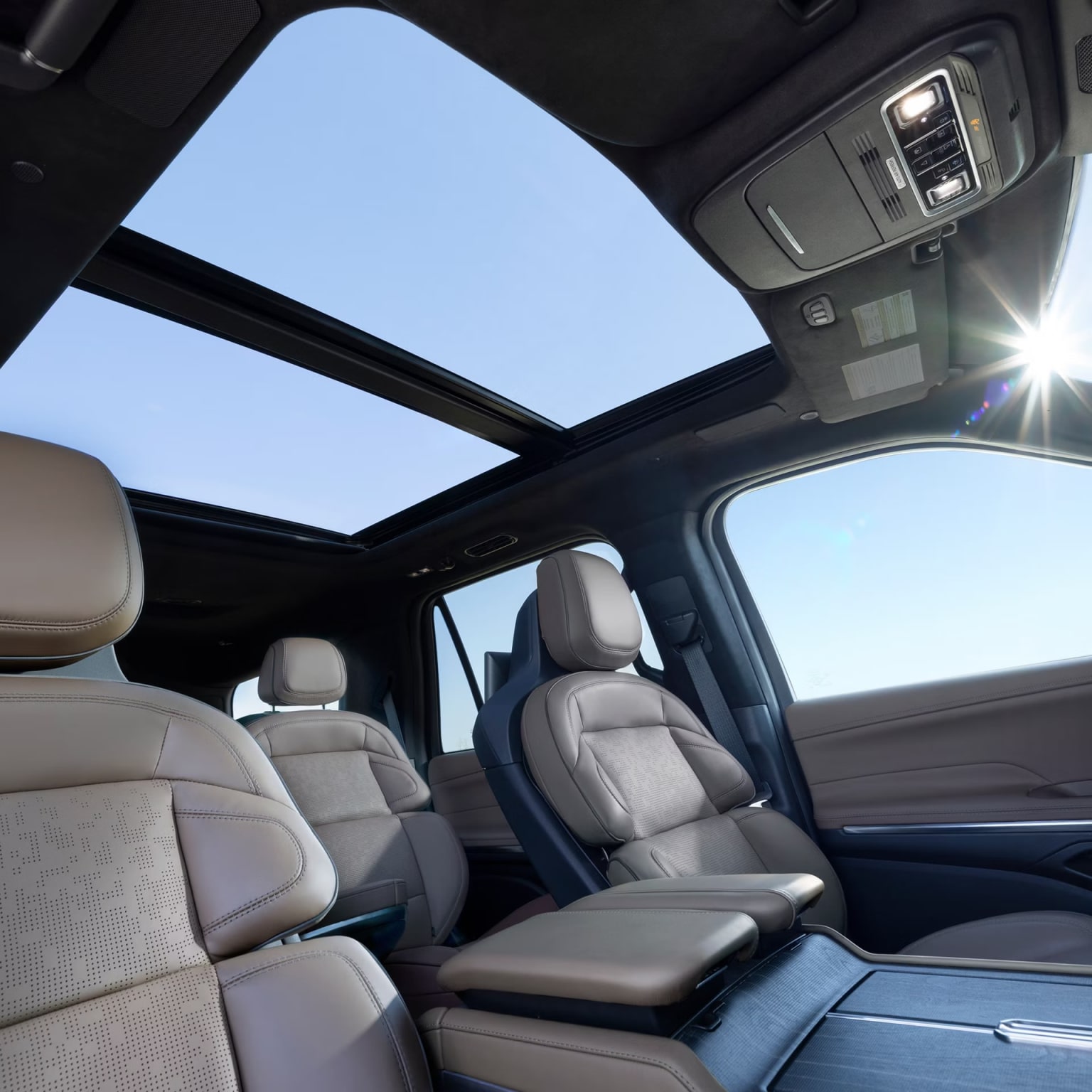 Interior view of a vehicle with a panoramic sunroof, light-colored upholstered seats, dashboard, and center console.