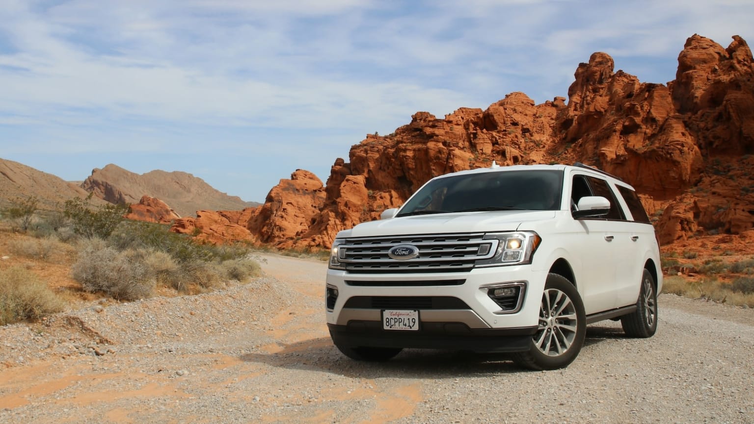 a white ford expedition vehicle parked on a gravel road in front of a rocky outcropping in the desert