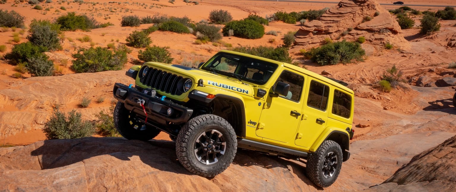 A yellow SUV is parked on a rocky hillside with a mountain in the background.