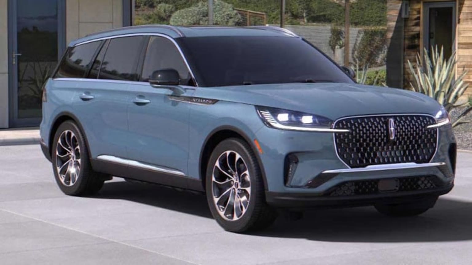A light blue SUV is parked in front of a modern house with landscaping.