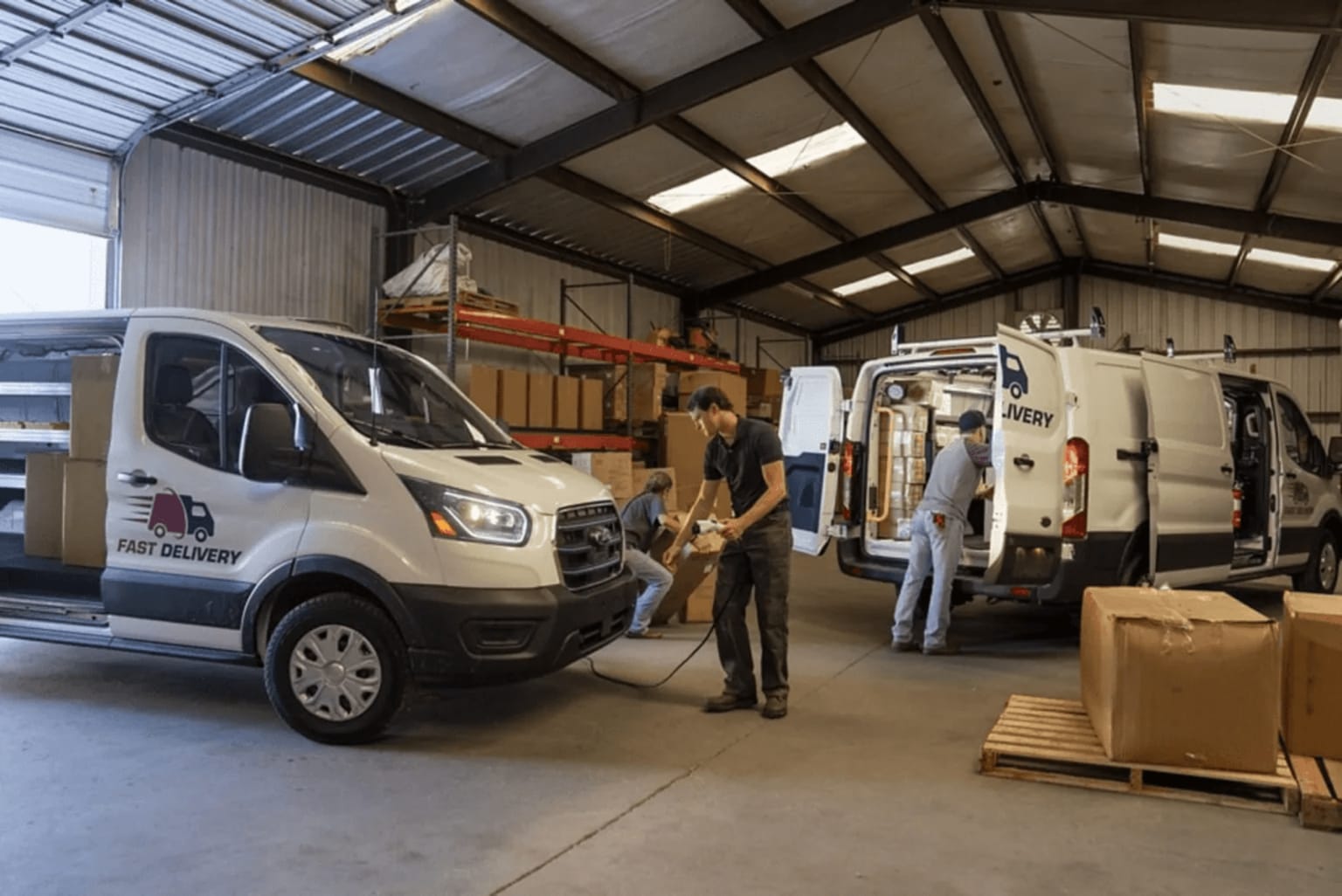 Interior of a warehouse with a white delivery van and several people working, surrounded by shelves and boxes.