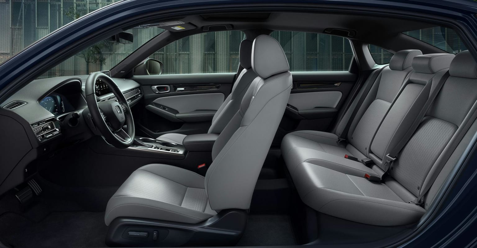 Gray leather interior of a car, including the driver's seat, steering wheel, and rear seats, with a blurred view of a building in the background through the car's windows.