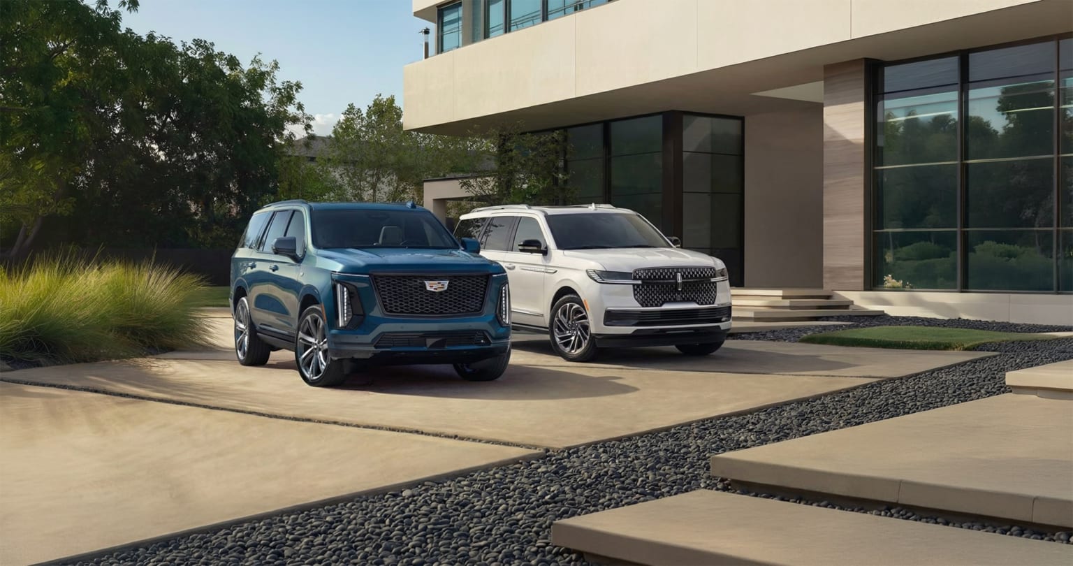 Lincoln Navigator and Cadillac Escalade full-size luxury SUVs parked outside modern home