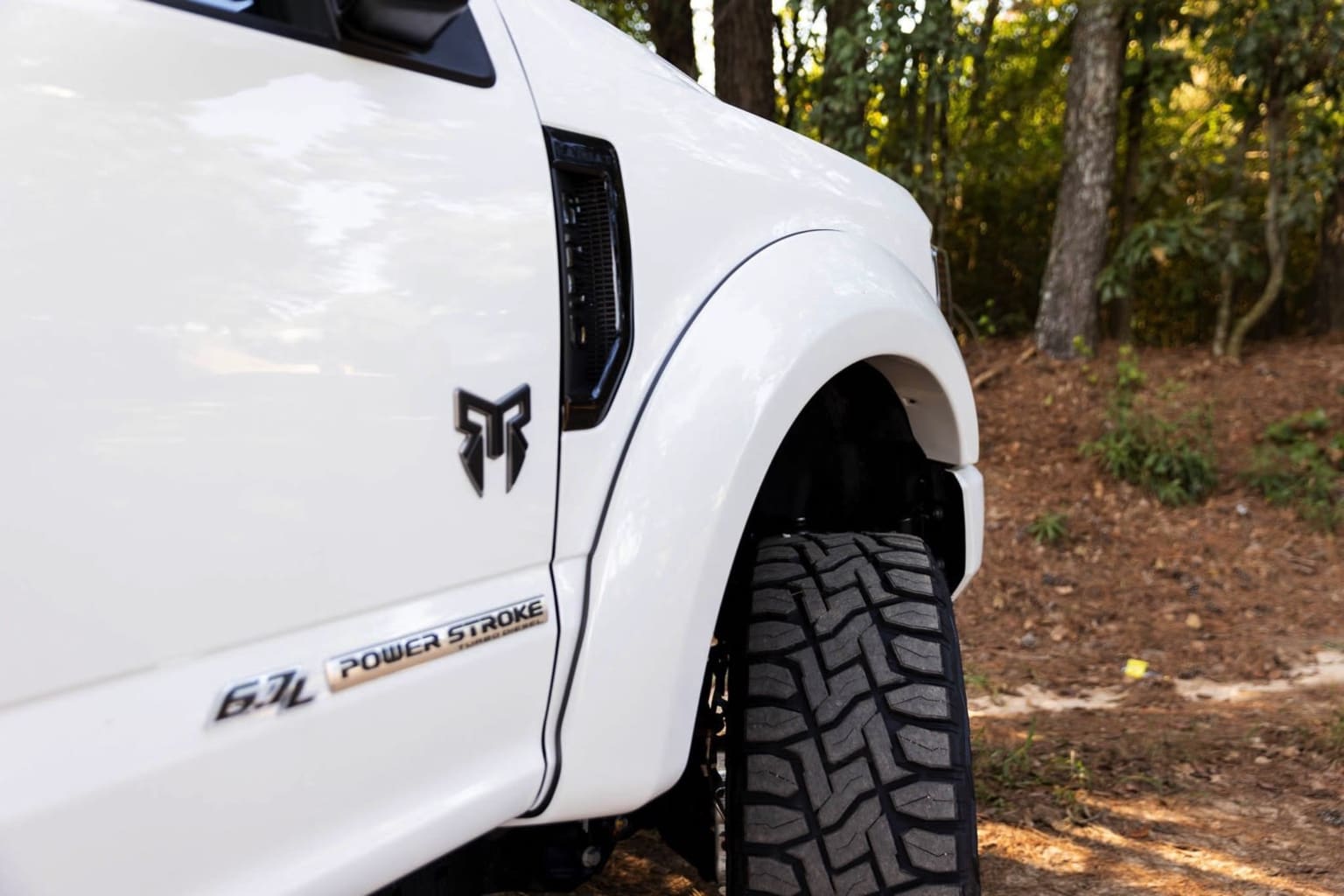 An off-road vehicle with large tires parked in a forested area, surrounded by trees and foliage.