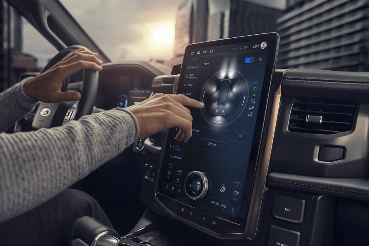 Hands operating a touchscreen display in the center console of a vehicle, with the interior of the car visible in the background.