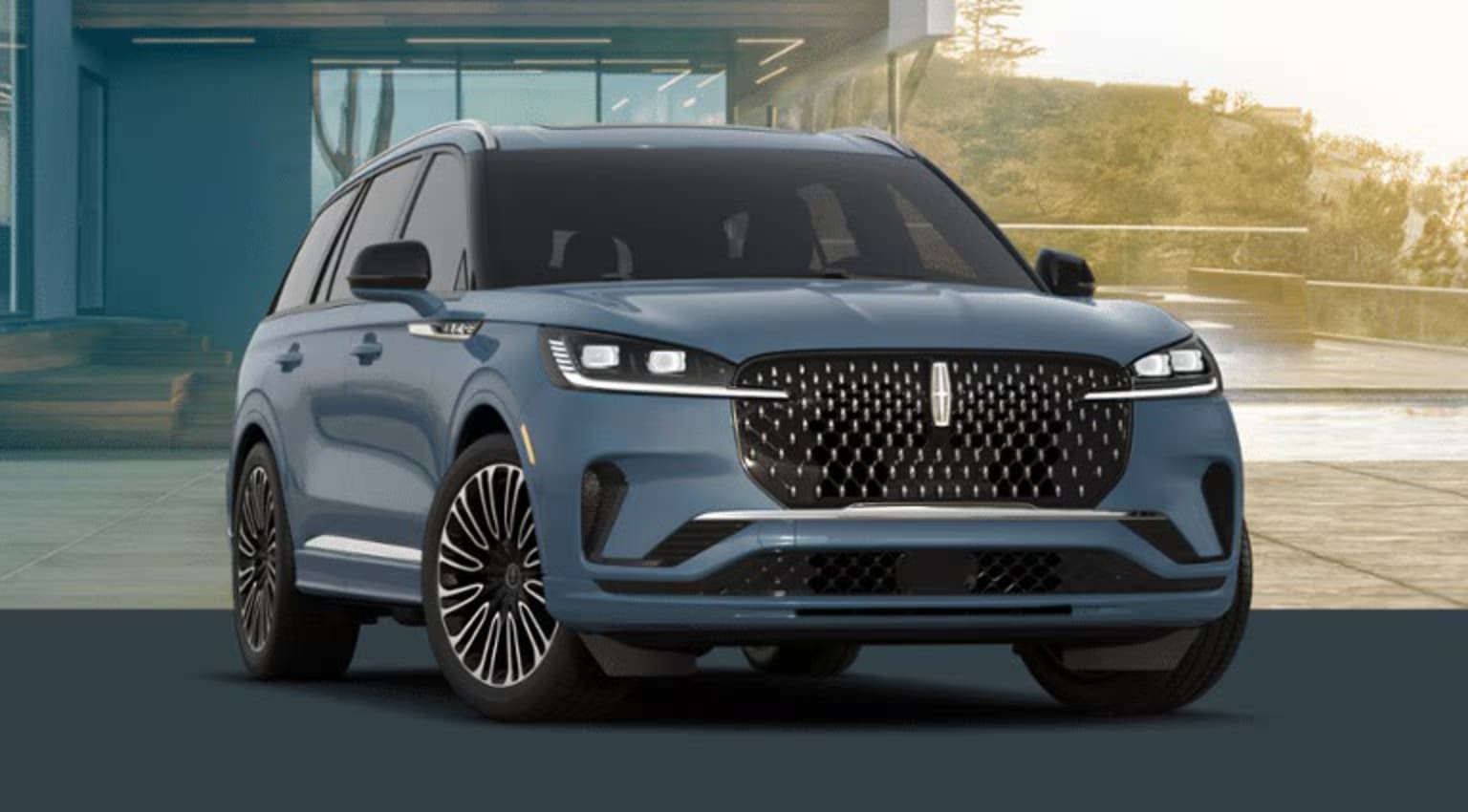 A sleek, dark-colored SUV with a prominent grille and distinctive headlights is parked in front of a modern, glass-fronted building, with the sun's rays casting a warm glow on the scene.