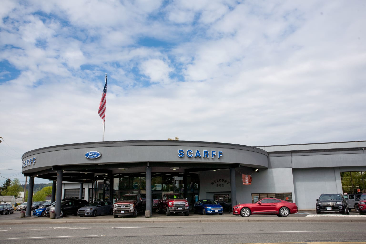 A car dealership with multiple vehicles displayed in front of a cloudy blue sky in the background.
