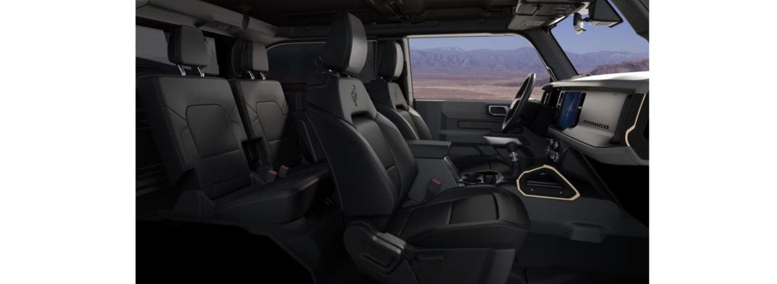 Interior of a spacious vehicle with multiple rows of comfortable-looking seats and a large windshield offering a scenic view of a mountainous landscape in the background.